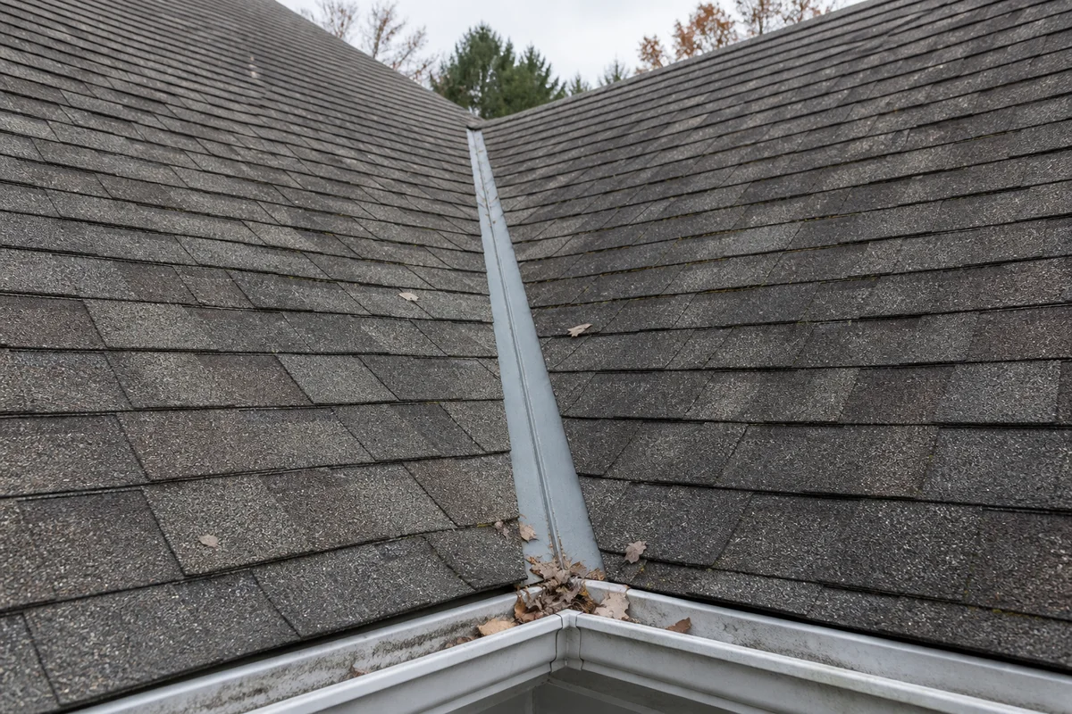 AI-generated illustration: A roof valley with aging shingles, metal flashing, and leaves near the gutter.